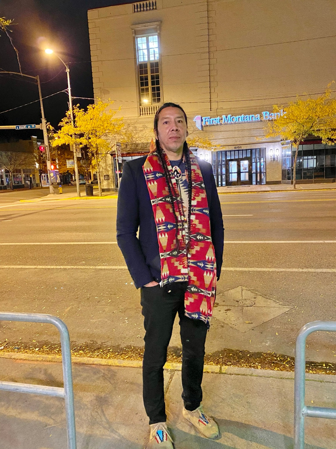 Teague WestWolf GoodVoice wearing a patterned scarf in downtown Missoula at night