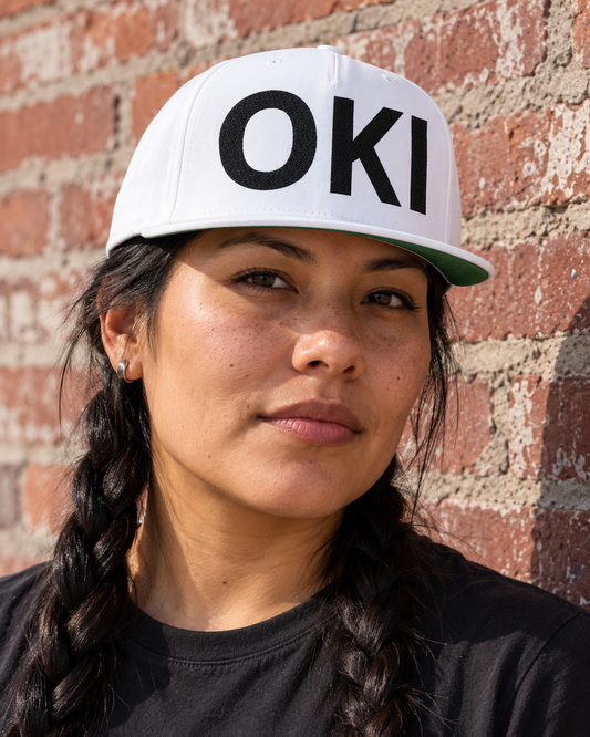 AI-generated lifestyle image of OKI /Hello in Blackfoot language - Embroidered Flat Bill Cap — Black Glitter Lettering Snapback